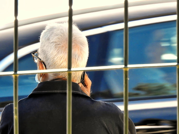 White-haired man talking on the phone near a fence - Fotoğraf, Görsel