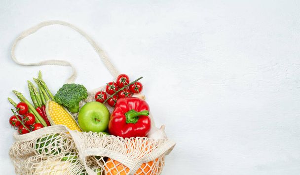 sac en maille réutilisable avec des légumes et fruits frais sur fond béton léger - Photo, image