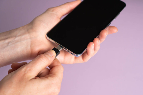 Mobile smart phones charging. Woman hands plugging a charger in a smart phone on violet background - Photo, Image