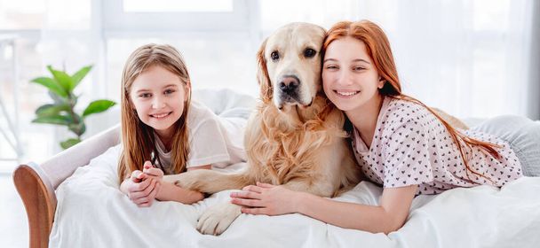 Chicas con perro golden retriever en la cama - Foto, imagen