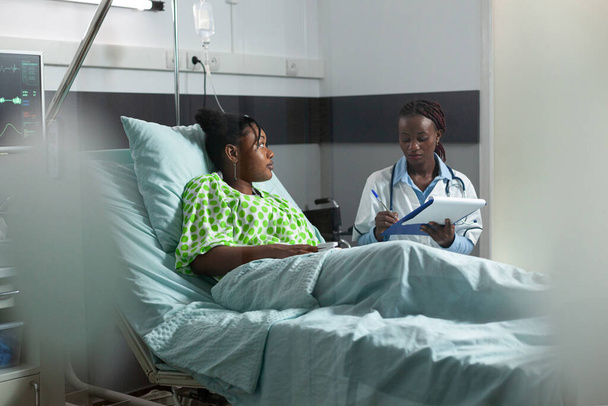 Adulto joven afroamericano con enfermedad que habla con el médico - Foto, imagen