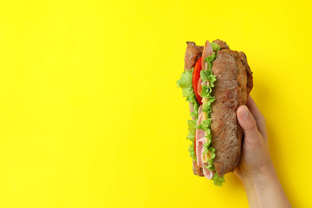 Weibliche Hand hält Ciabatta-Sandwich auf gelbem Hintergrund - Foto, Bild
