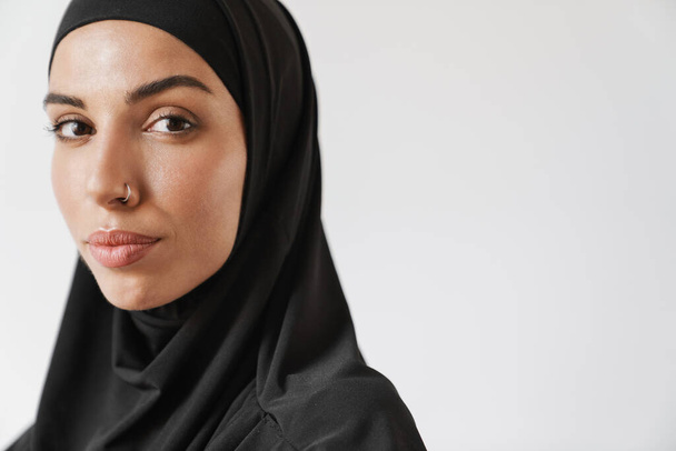 A close-up view of the muslim woman in hijab looking at the camera in the white studio - Foto, afbeelding