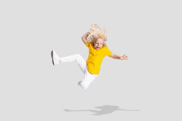 Cute little curly preschool boy having fun, playing isolated over white studio background. - Zdjęcie, obraz