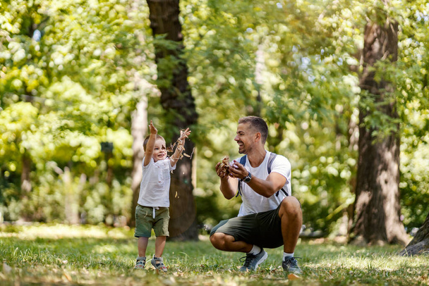Glückliche Kindheit und Erwachsenwerden. An einem Sommertag spielen Vater und Sohn in derselben Kleidung im Wald. Sie werfen Blätter in die Luft und lachen sich aus. Flucht in die Natur für Familienwochenende - Foto, Bild