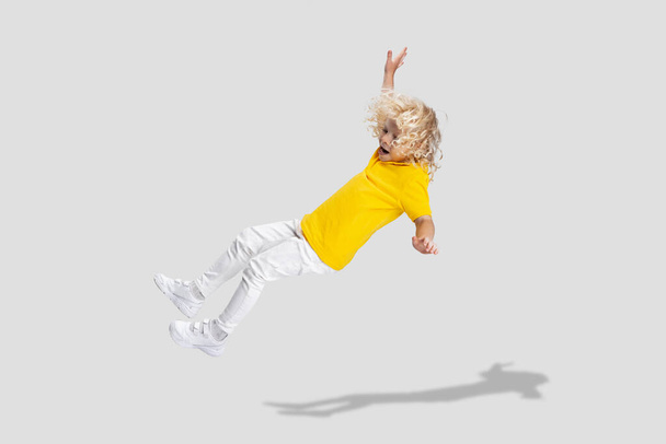 Cute little curly preschool boy having fun, playing isolated over white studio background. - 写真・画像
