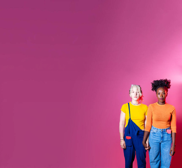 Isolated caucasian and black woman posing together holding hands for inclusion and tolerance on advertising copyspace background - Foto, afbeelding