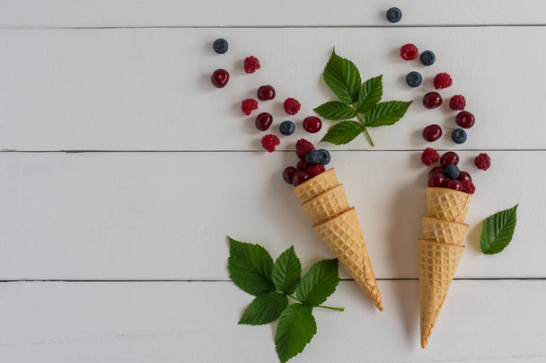 Fresh blueberry, cherry and raspberry in waffle cone on wooden white background. Top view. - Photo, image