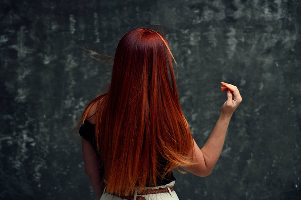 Red-haired Caucasian girl model with long curly hair on a gray background. Back view - Zdjęcie, obraz