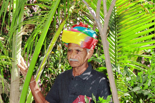 Detailní portrét staršího indického hinduistického farmáře, který má na zahradě turban, usmívá se a dívá se do kamery. Malý asijský farmář se usmívá na zahradě - Fotografie, Obrázek