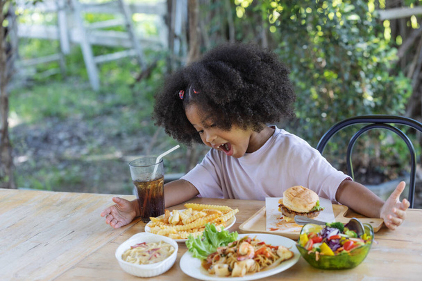 Gyermekkor és egészséges koncepció - Kis afro-amerikai göndör haj lány izgatott a különböző ételek az asztalon. - Fotó, kép