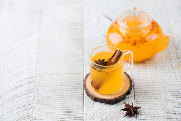 Autumn sea buckthorn tea in a mug with a cinnamon stick and in a teapot on a white wooden background. Autumn mood. - Foto, afbeelding