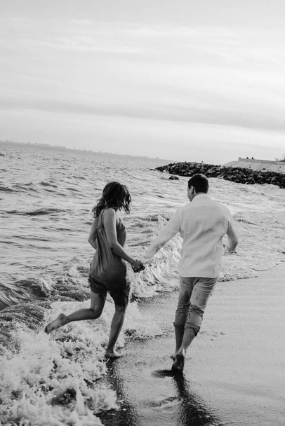 幸せな若いヨーロッパのカップルの肖像画は海岸沿いに走っています。幸せな生活様式。白黒写真 - 写真・画像