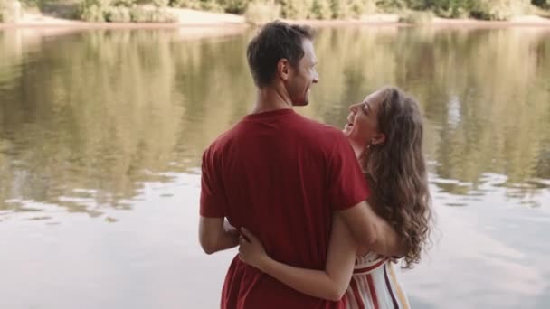 森の湖の前に立って、話をし、お互いの目を見て、美しいコーカサスの英雄のカップルの抱擁の背面ビュー - 映像、動画