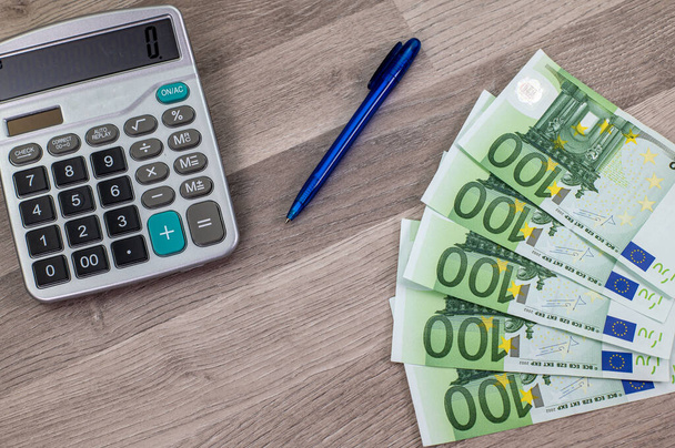 stylo calculateur et billets de 100 euros sur une table en bois - Photo, image