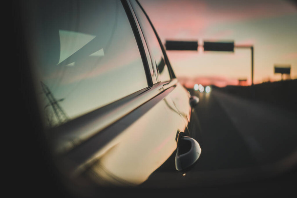 Rückspiegel spiegelt den Sonnenuntergang und verschwommene Autoscheinwerfer auf der Autobahn - Foto, Bild