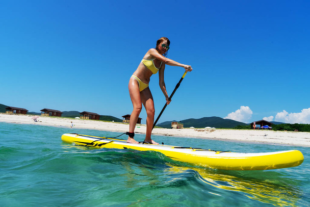 Woman stand up on paddle board in sea. Big yellow board in turquoise water. - Zdjęcie, obraz