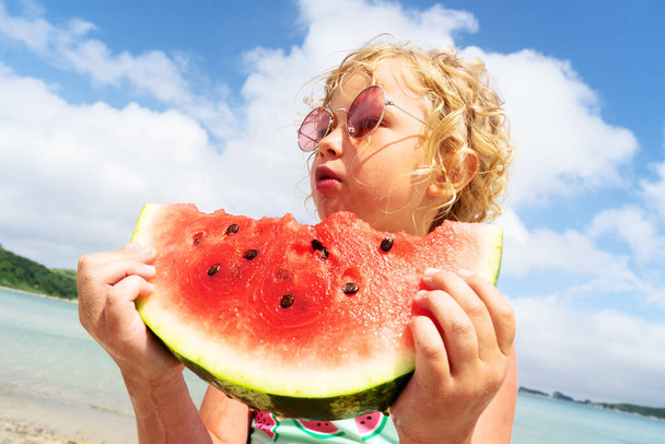 Portrait little girl licking fresh watermelon slice posing on beach having fun and positive emotion - 写真・画像