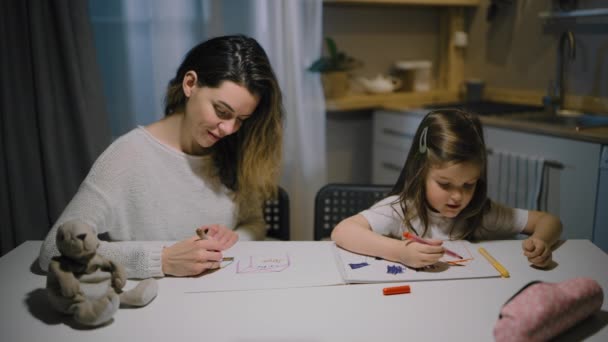 Uma mãe e uma pequena filha desenhar desenhos em papel na cozinha com marcadores - Filmagem, Vídeo