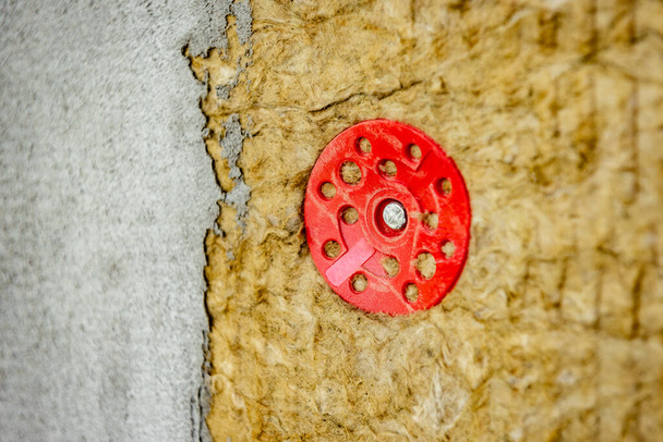 Листы зеленой минеральной ваты прикрепляются к стене с дюбелями с красными пластиковыми колпачками. Фаза строительства.  - Фото, изображение
