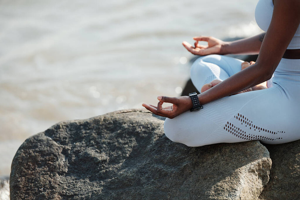 Imagen de cerca de una mujer en forma sentada en posición de loto disfrutando de su tranquila meditación en la playa - Foto, Imagen