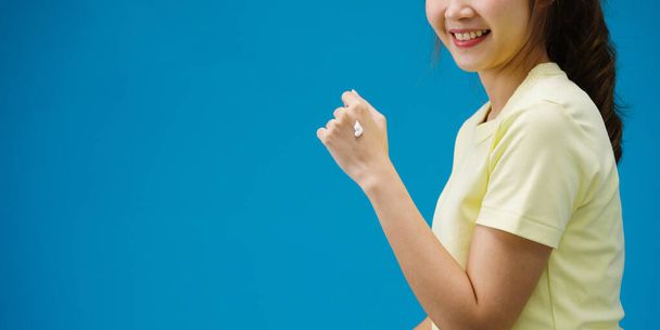 Giovane ragazza asiatica applicando crema protettiva sulle mani isolate su sfondo blu. Copia spazio per inserire un testo, un messaggio per la pubblicità. Area pubblicitaria, contenuti promozionali mockup. - Foto, immagini