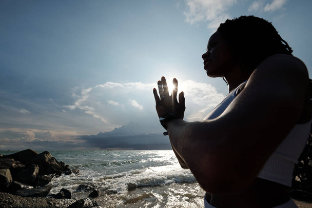 Lovely fit young sportswoman doing namaste mudra when meditating in rays of setting sun - Photo, Image