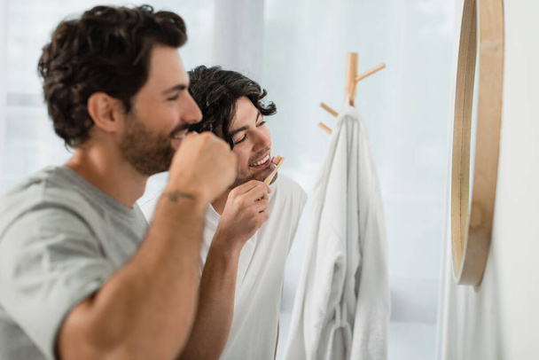 feliz gay pareja cepillado dientes cerca espejo en cuarto de baño - Foto, Imagen