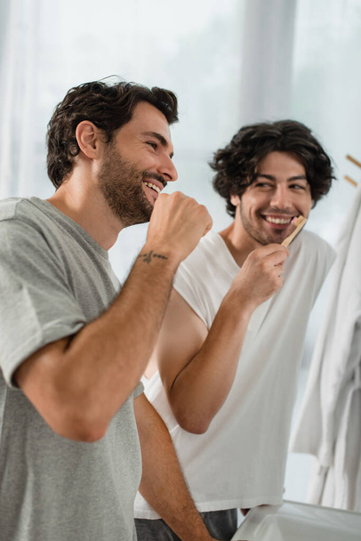 позитивная пара геев чистят зубы в ванной комнате - Фото, изображение