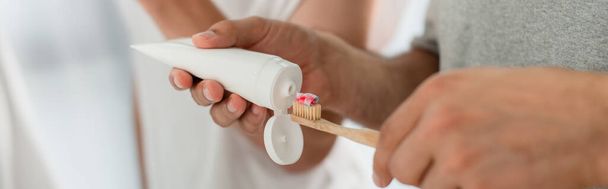 vista recortada del hombre apretando la pasta de dientes en el cepillo de dientes cerca de novio en el baño, pancarta - Foto, Imagen