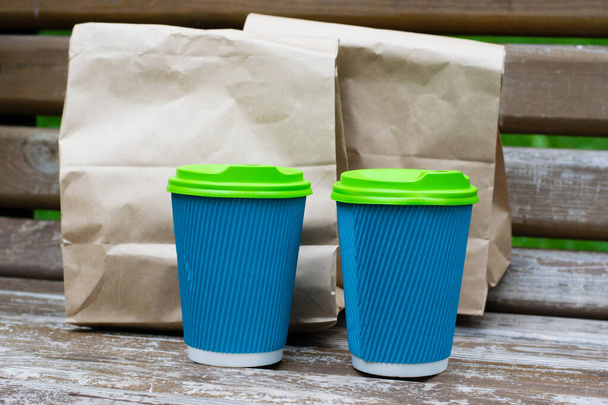 Bolsa de papel con comida para llevar y vasos con café en un banco en el parque. Concepto de entrega de alimentos, comunicación durante la cuarentena covid 19. - Foto, Imagen