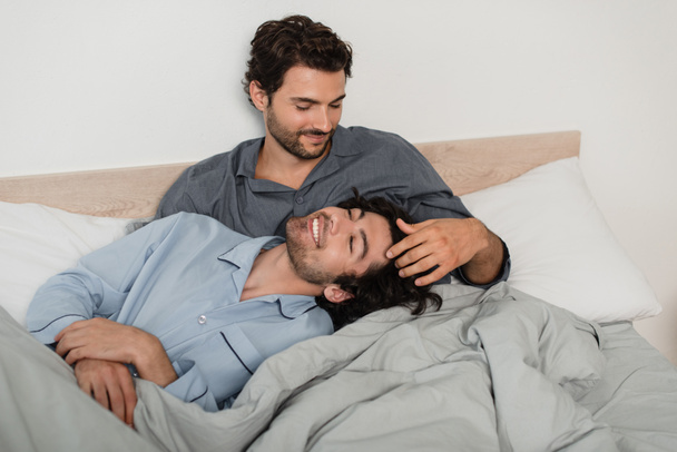 gay l'homme caressant cheveux de copain dans lit - Photo, image