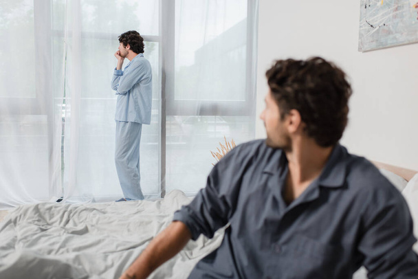 man standing and looking at window with blurred boyfriend on foreground, relationship difficulties concept - Фото, зображення