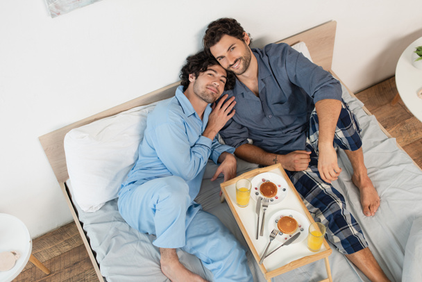 górny widok gej para uśmiech w pobliżu taca z śniadanie na łóżko - Zdjęcie, obraz
