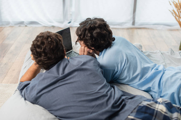 indietro vista di gay coppia guardando film su laptop in letto - Foto, immagini