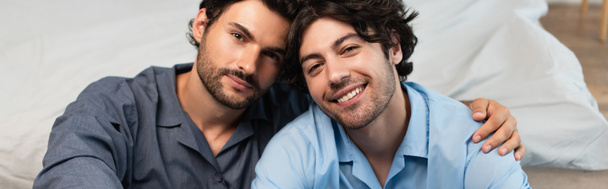 χαρούμενο νεαρό γκέι ζευγάρι που αγκαλιάζεται στην κρεβατοκάμαρα, πανό - Φωτογραφία, εικόνα