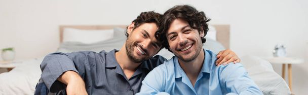 positive young gay couple hugging in bedroom, banner - Фото, изображение