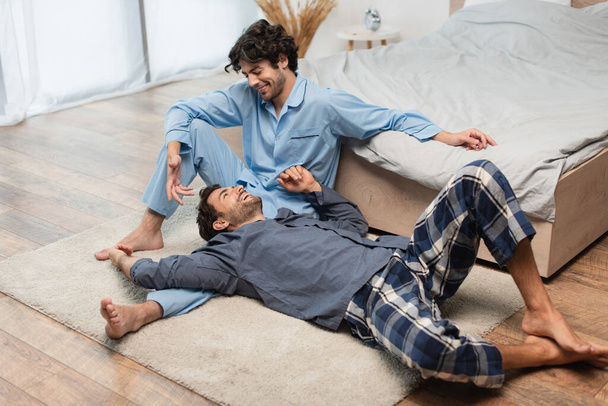 ευχαριστημένος gay άντρας ξαπλωμένος στα γόνατα του φίλου του στην κρεβατοκάμαρα  - Φωτογραφία, εικόνα