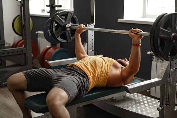 Bearded man bodybuilder doing bench press exercise in gym - Fotó, kép