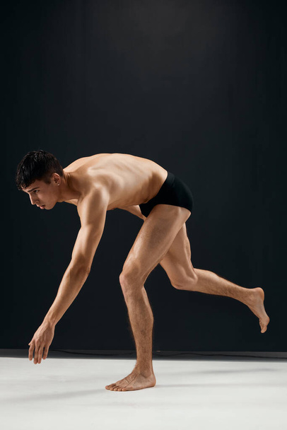 man bodybuilder in black shorts bent knees dark background - Φωτογραφία, εικόνα