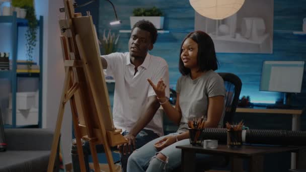 Αφροαμερικανοί καλλιτέχνες ζευγάρι έλεγχο τέχνης σχέδιο στο καβαλέτο - Πλάνα, βίντεο