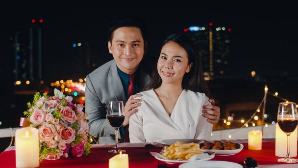 若いアジアのカップルは、甘い瞬間を祝う記念日と都市の夜の屋上レストランでロマンチックなディナーで幸福の瞬間を記念して写真を撮ります。愛の関係、結婚の概念. - 写真・画像