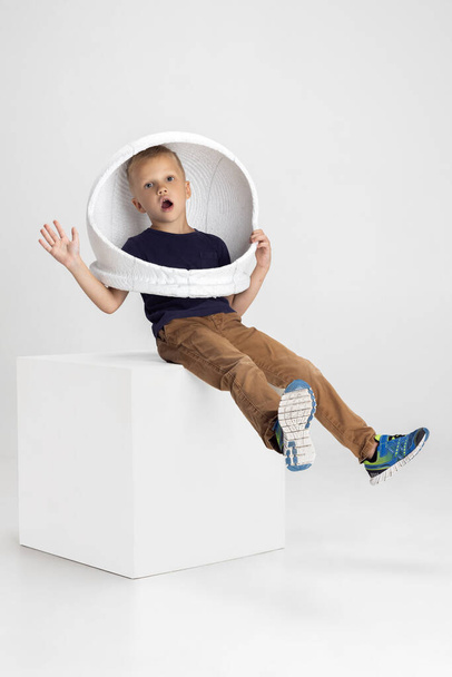 Portrait of school boy, pupil in big helmet isolated on white studio background. Copyspace for ad. Childhood, education, emotion concept. Little astronaut - Foto, afbeelding