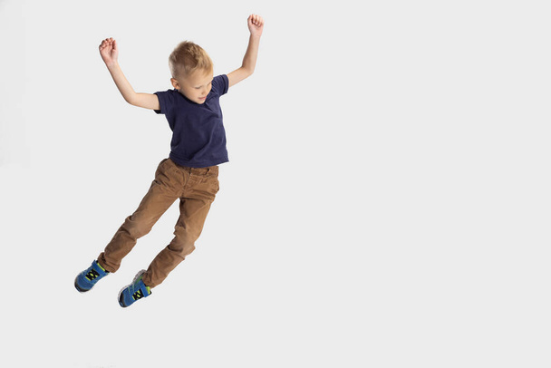 Portrait of school boy, pupil falling down isolated on white studio background. Copyspace for ad. Childhood, education, emotion concept. - Fotó, kép