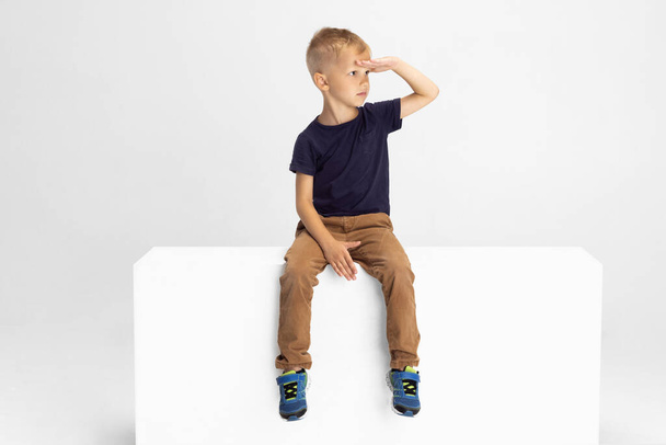 One preschool boy sitting on big box isolated on white studio background. Copyspace for ad. Childhood, education, emotion concept - Foto, immagini