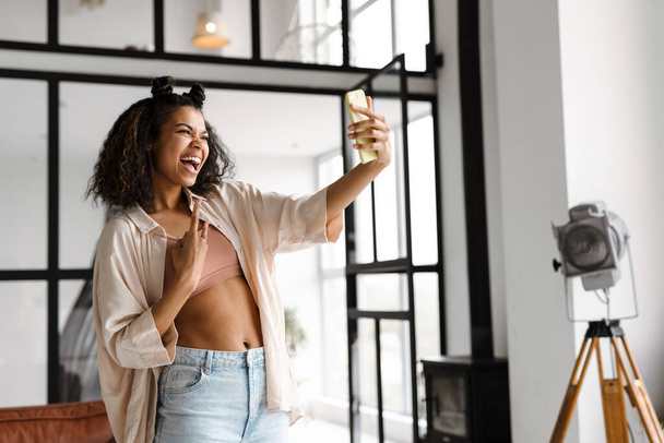 Giovane donna afroamericana felice in possesso di smart phone fare un vlog da casa - Foto, immagini
