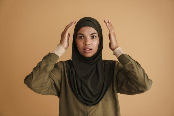 Black muslim woman in hijab expressing surprise at camera isolated over beige background - Foto, imagen