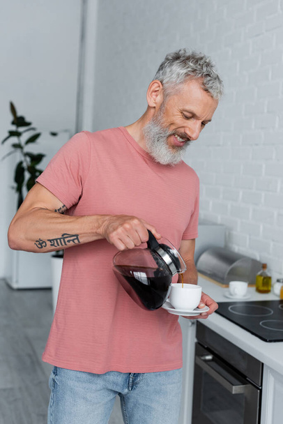 Smiling man pouring coffee in kitchen  - Valokuva, kuva