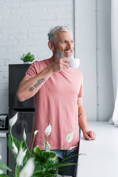 Mature man with coffee cup smiling in kitchen  - Foto, Imagem