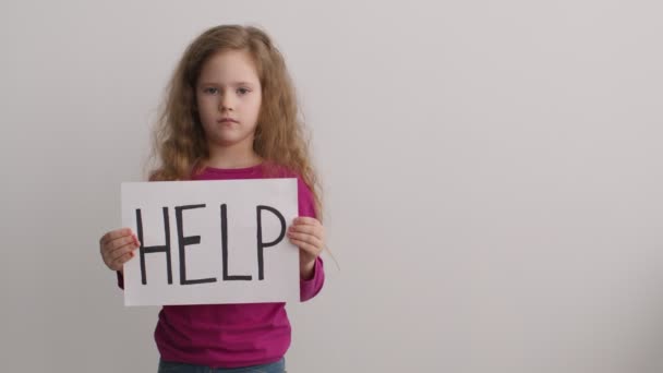 Piilevän perheväkivallan uhri. Söpö pieni tyttö poseeraa yli valkoinen seinä tausta ja pitämällä kyltti sanalla HELP - Materiaali, video